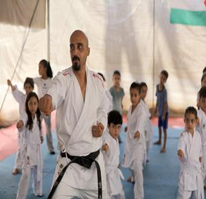 مدرب الفنون القتالية خليل عياد يشرف على تدريب مجموعة من الأطفال رياضة الكاراتيه بإمكانيات محدودة داخل خيمة نصبها في دير البلح وسط قطاع غزة، بعد تدمير نادي الزيتون الرياضي في مدينة غزة.