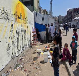 فنانون يرسمون جداريات وكتابات خطية على جدران مدرسة حُوّلت إلى مأوى للنازحين في مدينة غزة