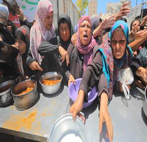 نازحون يصطفون تحت وهج الشمس انتظارا لتلقي وجبات غذائية مجانية من تكية خيرية في مدينة غزة