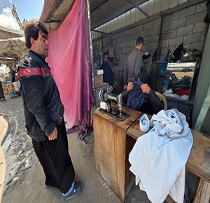 المسنّة نغين بن عيسى (77 عاما) تواصل حياكة الملابس داخل خيمة في خان يونس لتأمين مصدر دخل بعد أن فقدت كل ما تملك جراء الحرب